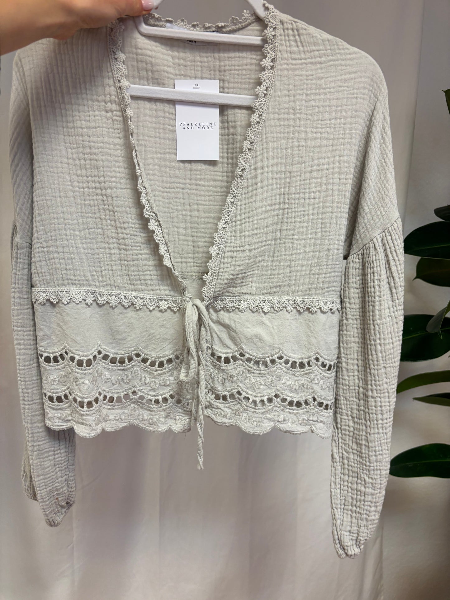 Musselinbluse zum Binden mit Spitzenverzierung ab der Taille vor weißem Hintergrund