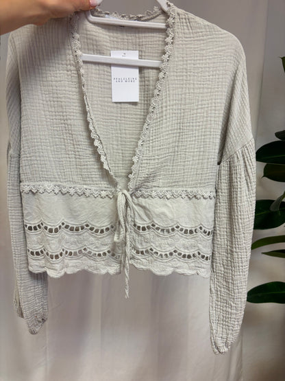 Musselinbluse zum Binden mit Spitzenverzierung ab der Taille vor weißem Hintergrund